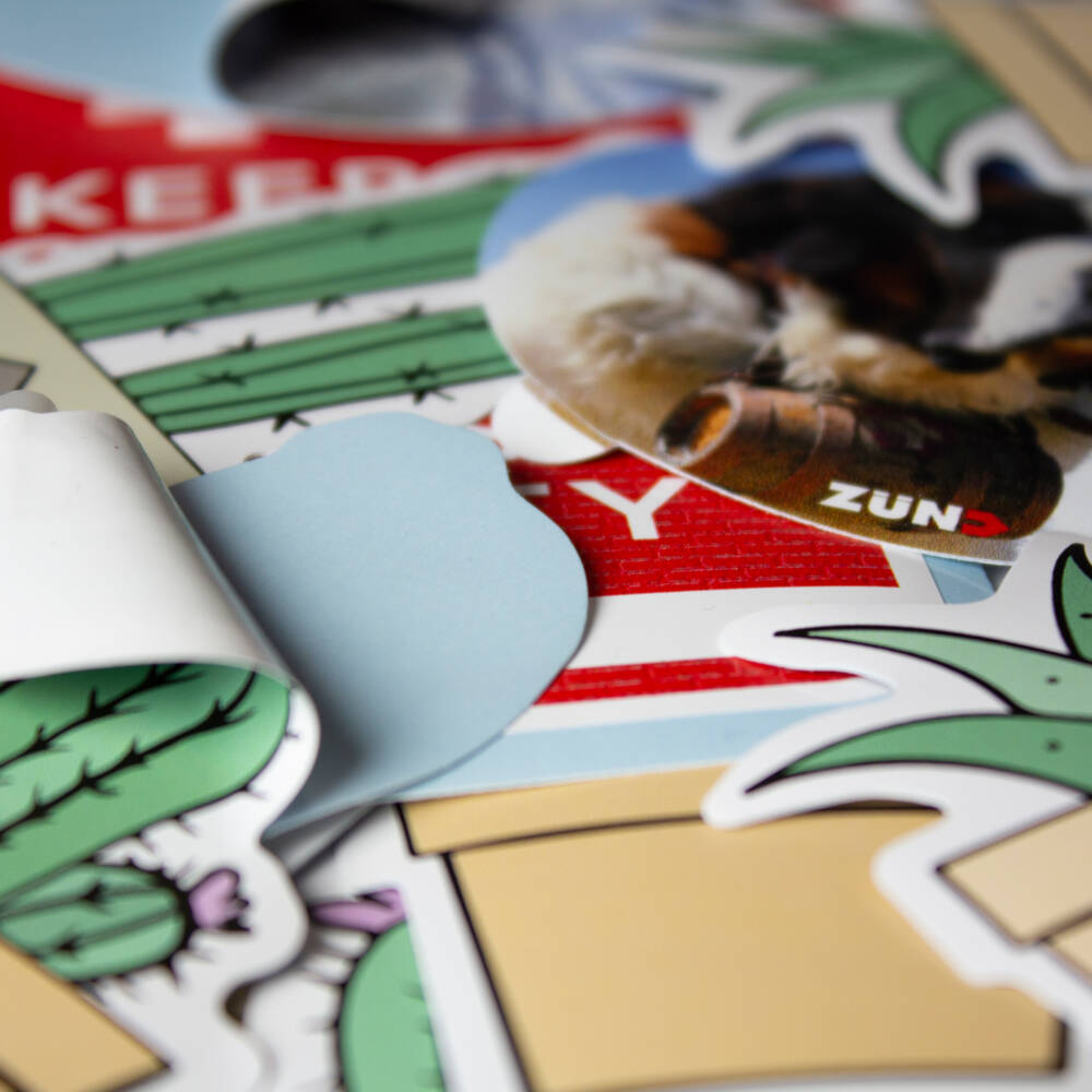 Um close-up de adesivos com o logotipo Zünd e desenhos de cactos e raios. Um close-up de adesivos com o logotipo Zünd e desenhos de cactos e raios.