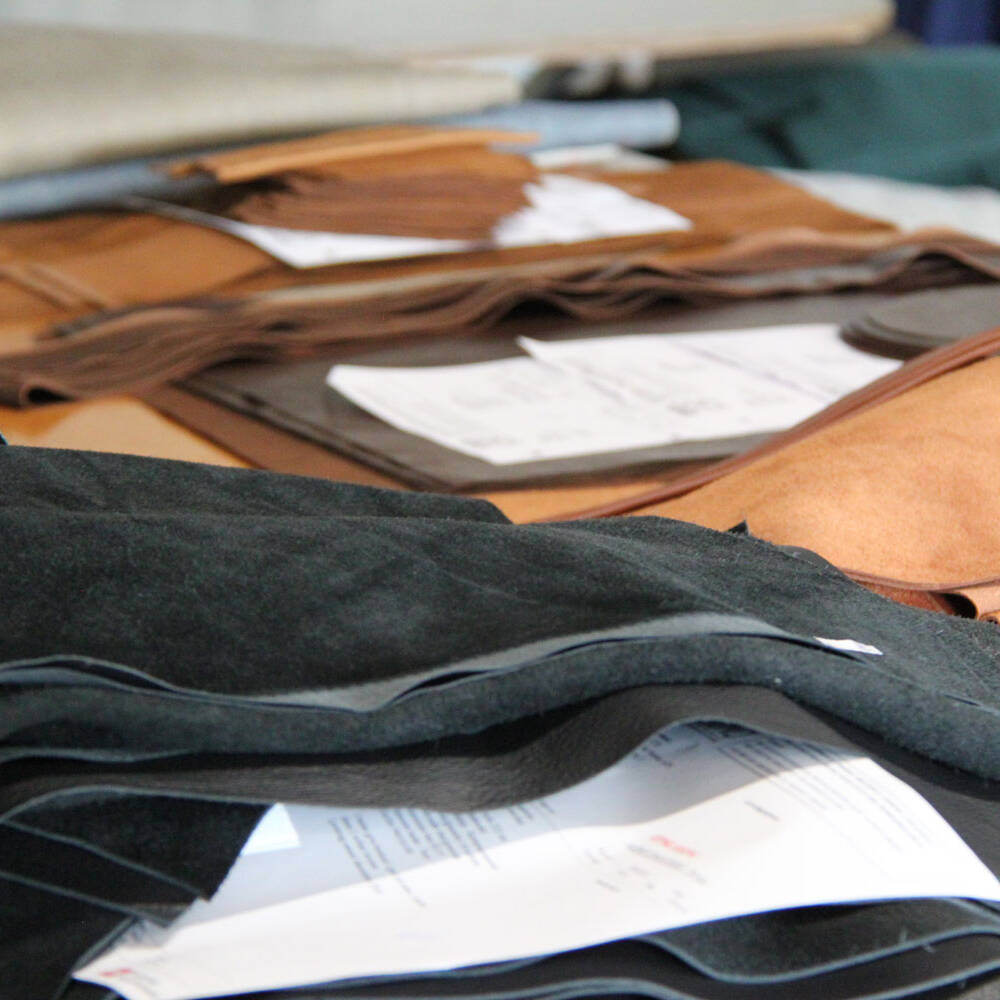 Stacks of black and brown leather swatches, some with paper underneath, suggesting material selection for manufacturing.