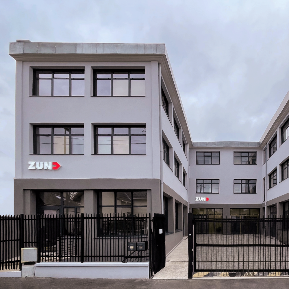 Bâtiment moderne de Zund France avec le logo de l'entreprise et une clôture noire devant. Bâtiment moderne de Zund France avec le logo de l'entreprise et une clôture noire devant.