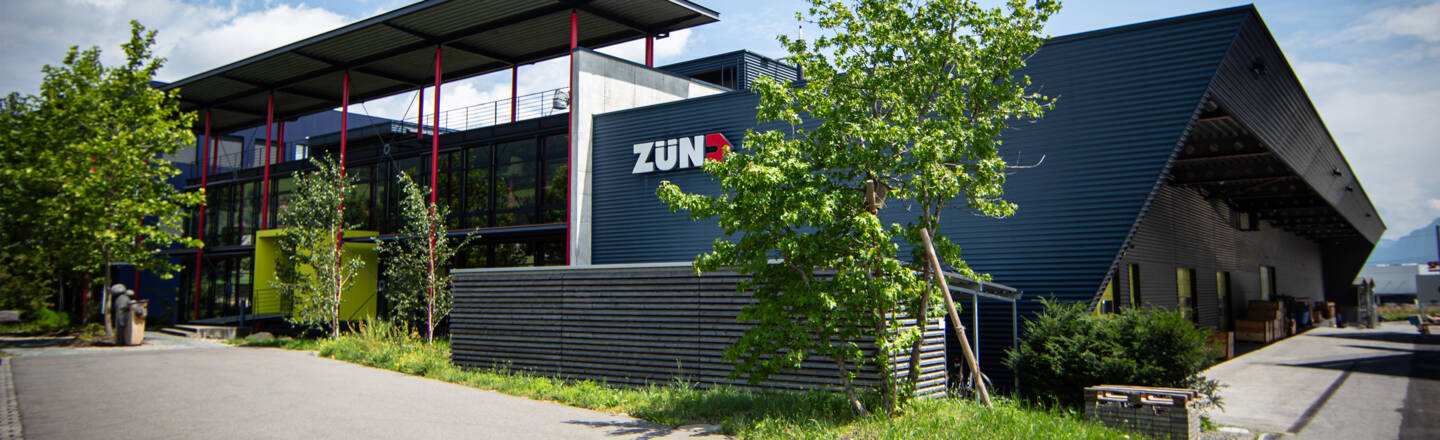 Das moderne Gebäude des Zünd Hauptsitzes mit großen Fenstern, roten Säulen und dem Zünd-Logo an der Fassade.