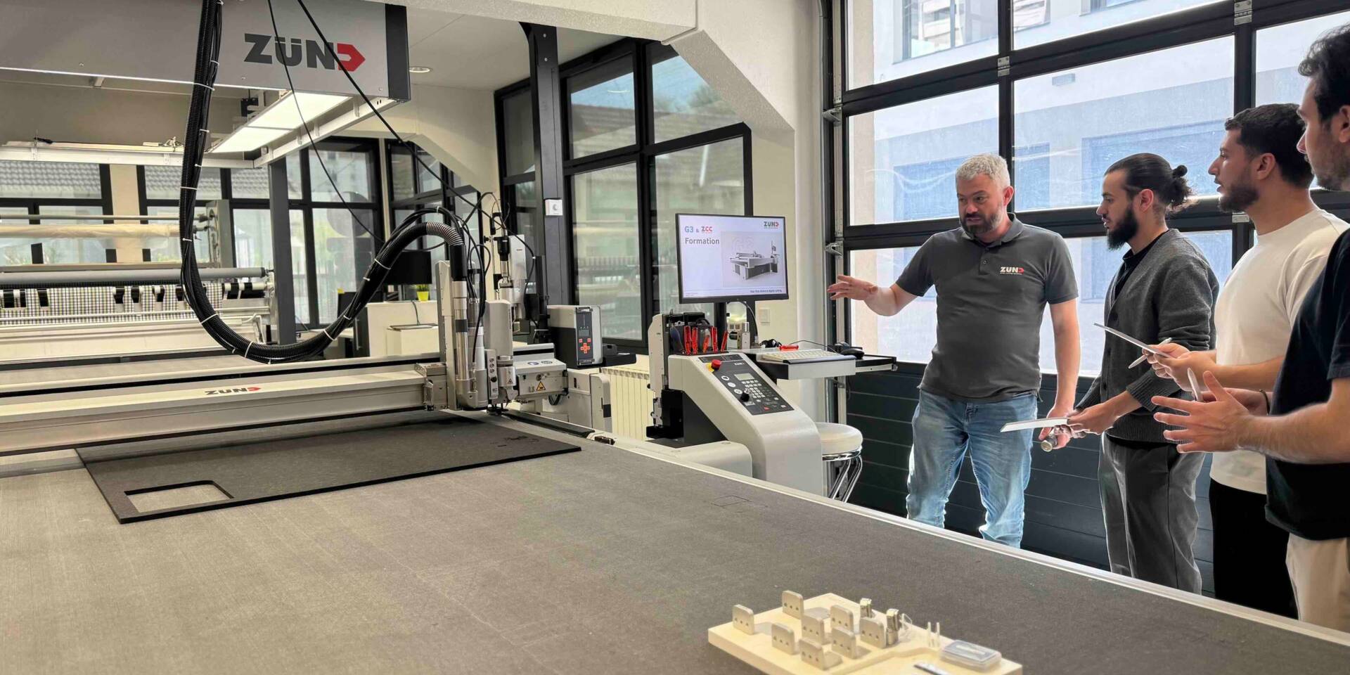 Session de formation Zund France dans le showroom de Vitry-sur-Seine : un formateur accompagne des opérateurs dans la prise en main d’une table de découpe numérique, en conditions réelles de production.