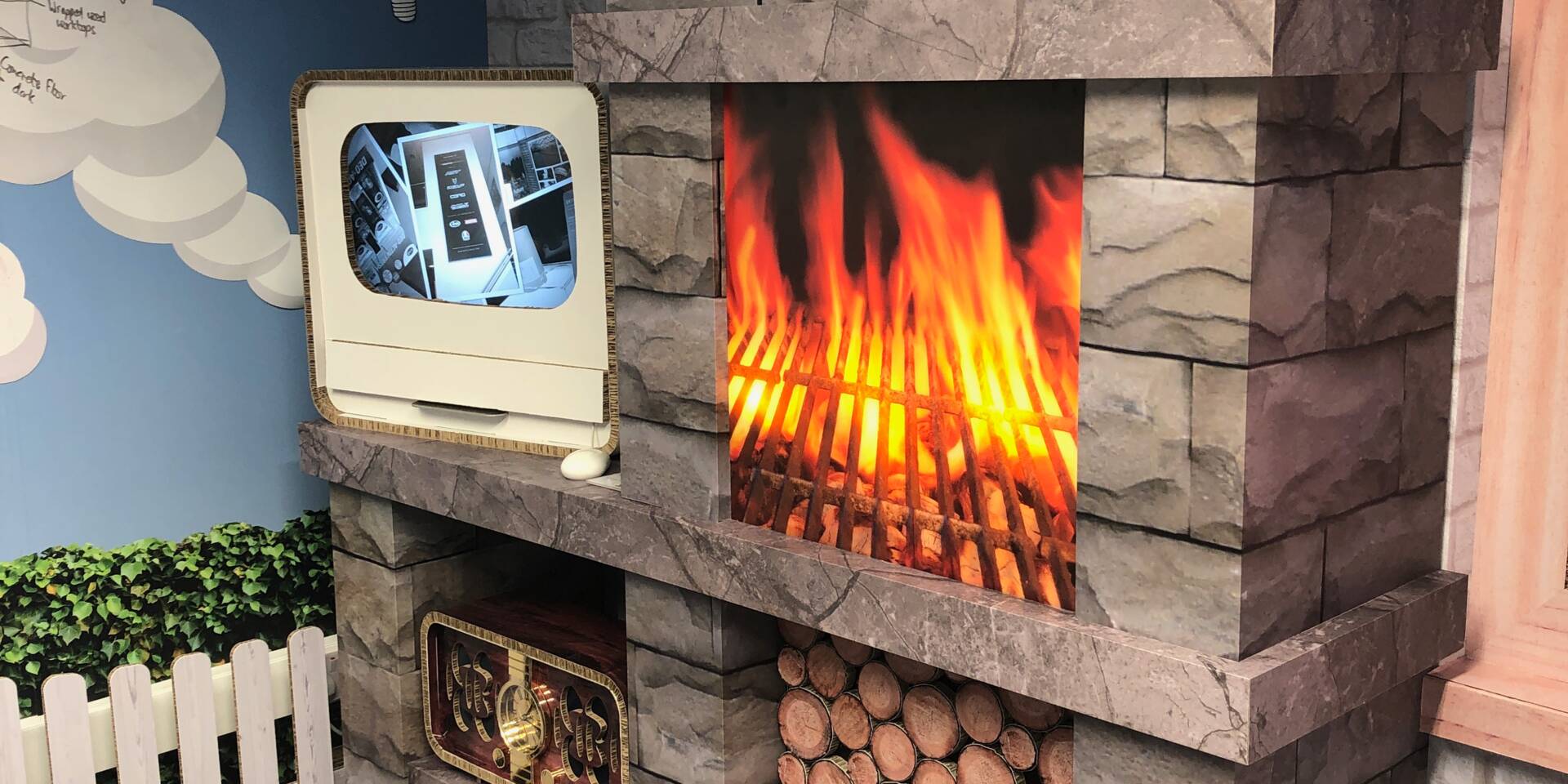 A decorative fireplace with a digital screen showing a product display, next to a vibrant flame graphic and stacked logs.