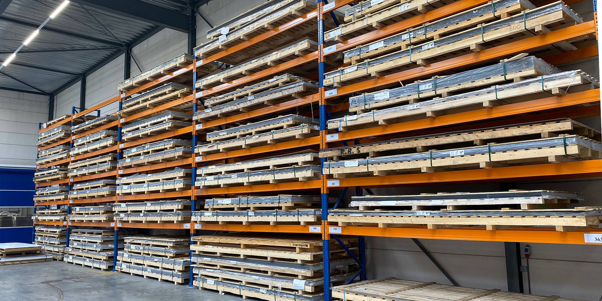 Groot magazijn met veel stellingen die gestapeld zijn met metalen platen op pallets. Zünd Systemtechnik.