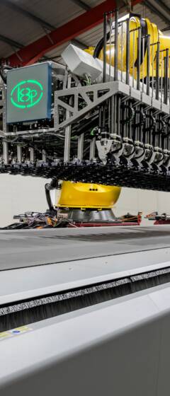 Automated cutting system with a robotic arm and a wide conveyor belt in a factory setting.