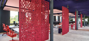 Modernes Büro mit roten Akustikpaneelen, Bürostühlen und Hängeleuchten unter einer violetten Decke.