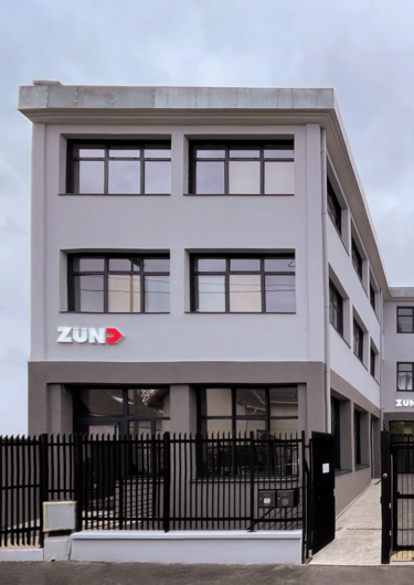Bâtiment moderne de Zund France avec le logo de l'entreprise et une clôture noire devant. Bâtiment moderne de Zund France avec le logo de l'entreprise et une clôture noire devant.