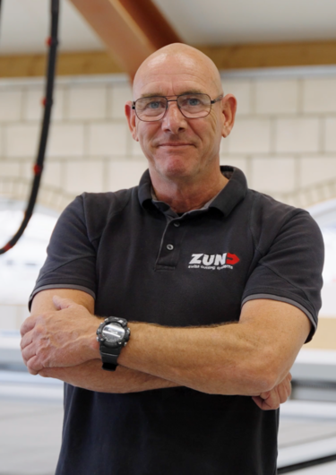 Three men in Zünd Systemtechnik uniforms stand in front of a black van outdoors. The Zünd logo is visible.