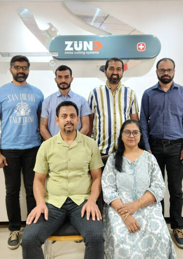 A group of five smiling individuals, likely employees, pose in front of a Zünd Swiss Cutting Systems logo.