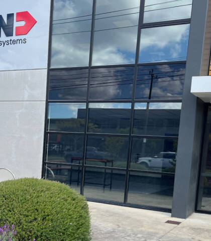 Z&uuml;nd Systemtechnik building exterior with large windows, modern facade, and lush greenery. The Z&uuml;nd logo is visible on the entrance door.