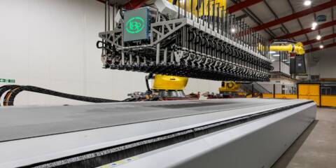 Automated cutting system with a robotic arm and a wide conveyor belt in a factory setting.