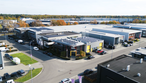 Fachada moderna do edifício Zünd Systemtechnik com logo e letreiro 'swiss cutting systems' sobre entrada amarela. Fachada moderna do edifício Zünd Systemtechnik com logo e letreiro 'swiss cutting systems' sobre entrada amarela.