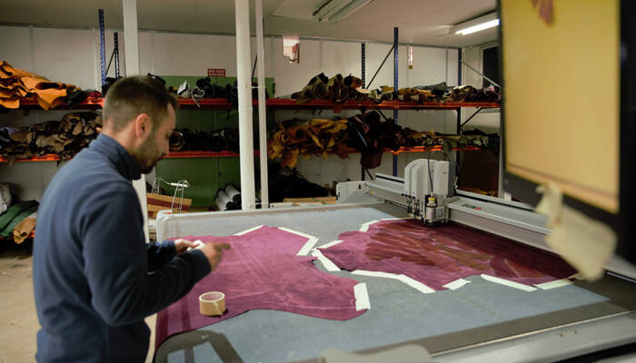 Un uomo lavora su un tessuto viola su un tavolo da taglio Zünd con un sistema di taglio automatico.