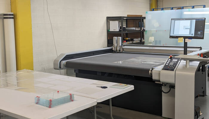 A Zünd digital cutting system with a computer monitor displaying software, ready for material processing in a workshop environment. A Zünd digital cutting system with a computer monitor displaying software, ready for material processing in a workshop environment.