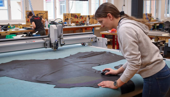 Digitale Präzision im Einsatz: Eine Sattlerin platziert eine Lederhaut für den Zuschnitt auf dem Zünd G3 Cutter. Mitarbeiterin positioniert eine Lederhaut auf dem Zünd G3 Cutter für den digitalen Zuschnitt.