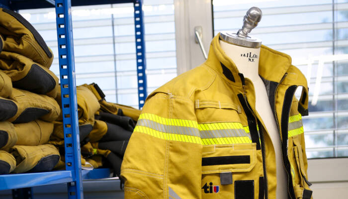 Gelbe Schutzjacke mit Reflexstreifen hängt auf Kleiderbügel in einem Lagerbereich.