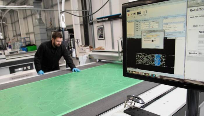 Operator in blue gloves works with a Zünd cutting system, monitoring the process on a computer screen displaying cutting patterns. Operator in blue gloves works with a Zünd cutting system, monitoring the process on a computer screen displaying cutting patterns.
