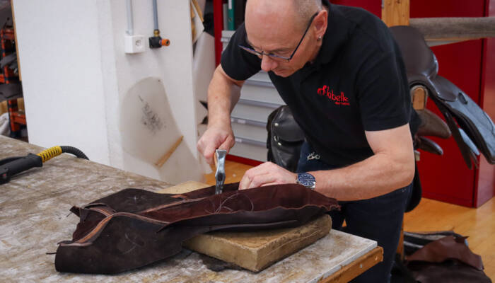 Sattler bearbeitet einen Sattel manuell mit einem Hammer.