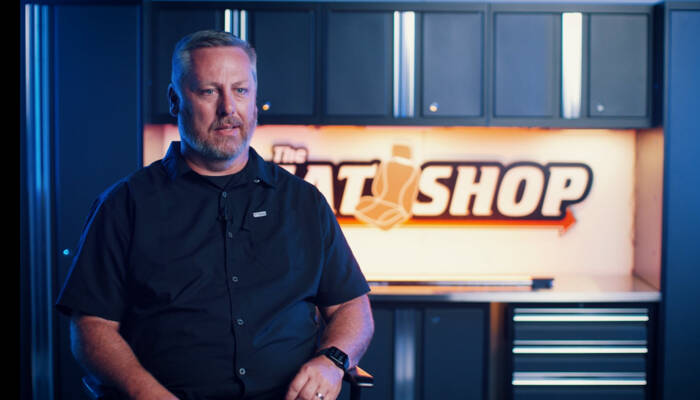 Ein Mann mit Bart in einem schwarzen Hemd sitzt vor einer Kulisse mit der Aufschrift 'THE SEAT SHOP'. Ein Mann mit Bart in einem schwarzen Hemd sitzt vor einer Kulisse mit der Aufschrift 'THE SEAT SHOP'.