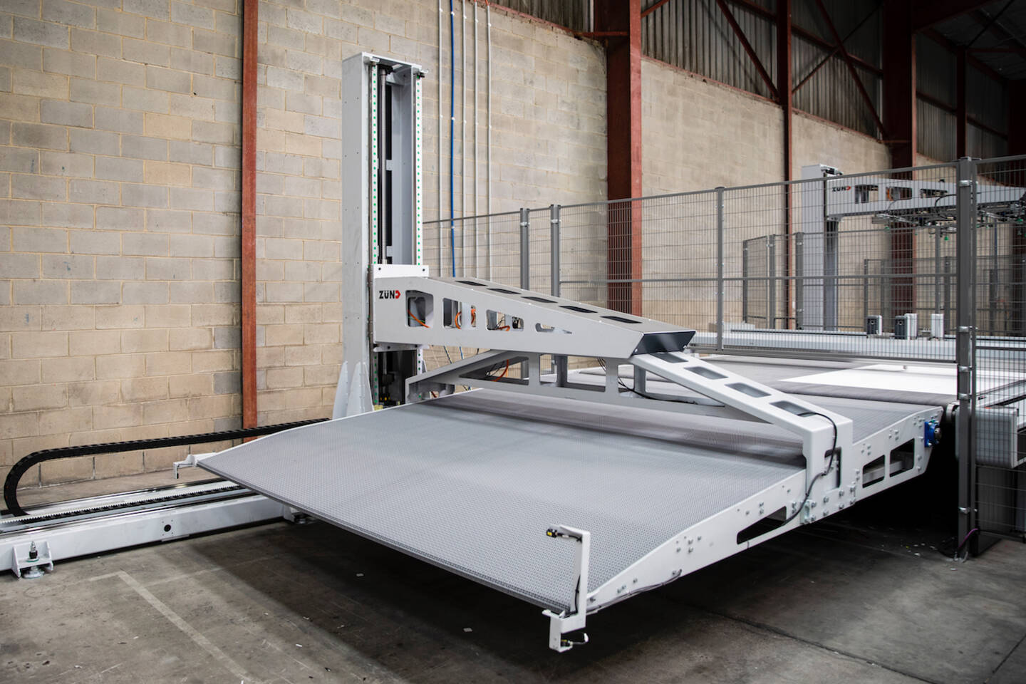 Automated Zünd G3 L-3200 cutting system with a conveyor belt and loading ramp in a warehouse setting. Automated Zünd G3 L-3200 cutting system with a conveyor belt and loading ramp in a warehouse setting.