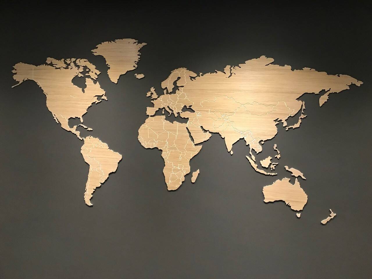 Een houten wereldkaart met gedetailleerde landsgrenzen, gemonteerd op een donkergrijze muur. Een houten wereldkaart met gedetailleerde landsgrenzen, gemonteerd op een donkergrijze muur.