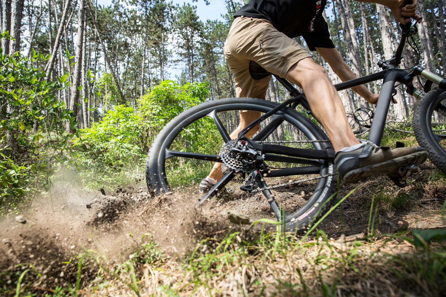 Mountainbiker rijdt op een bosweg, waarbij het achterwiel modder en aarde opslingert.