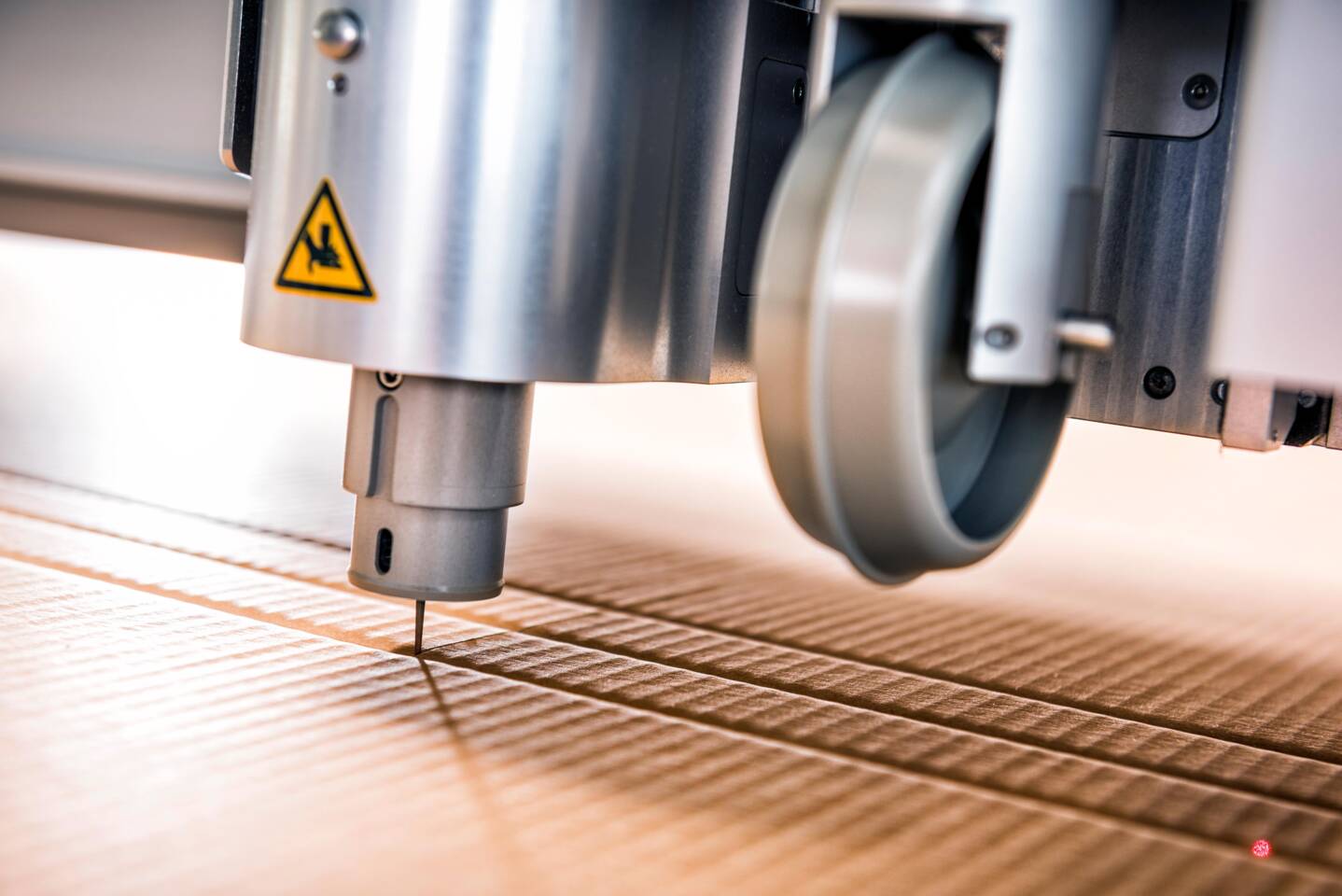 Ein Zünd G3 L3200 Cutter schneidet präzise durch eine Holzoberfläche mit parallelen Rillen. Ein Zünd G3 L3200 Cutter schneidet präzise durch eine Holzoberfläche mit parallelen Rillen.