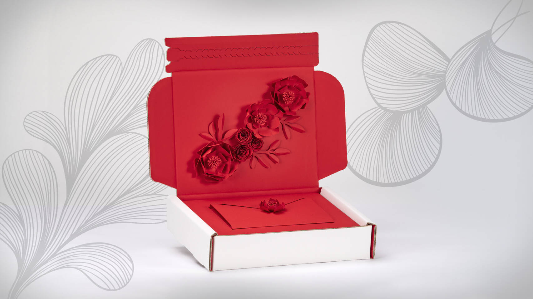 Scatola rossa aperta decorata con fiori di carta, contenente una busta con un fiore rosso.