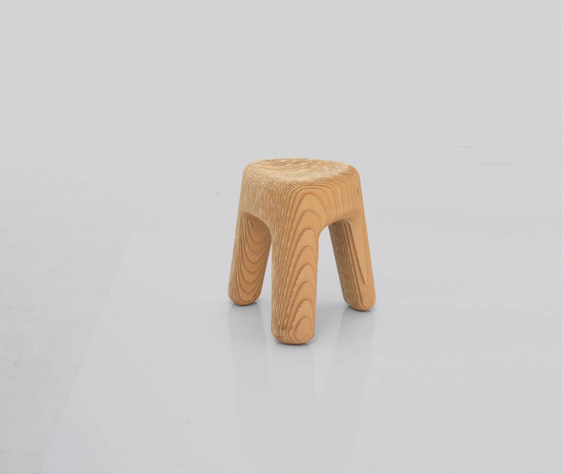 Tabouret rond en carton ondul&eacute;, avec quatre pieds incurv&eacute;s, pr&eacute;sent&eacute; sur un fond gris clair.