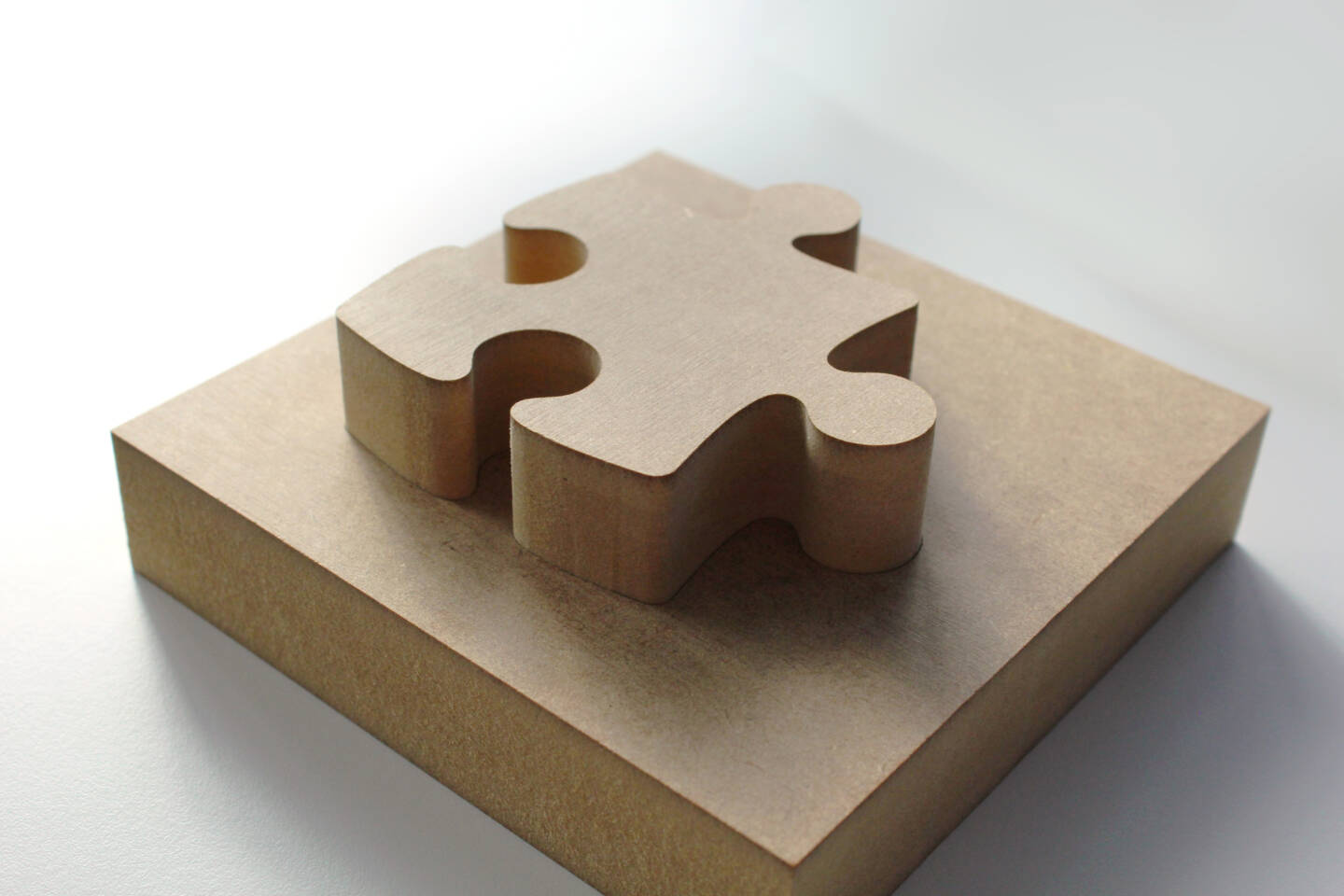 Un pezzo di puzzle in legno su una base quadrata di legno, su uno sfondo bianco.