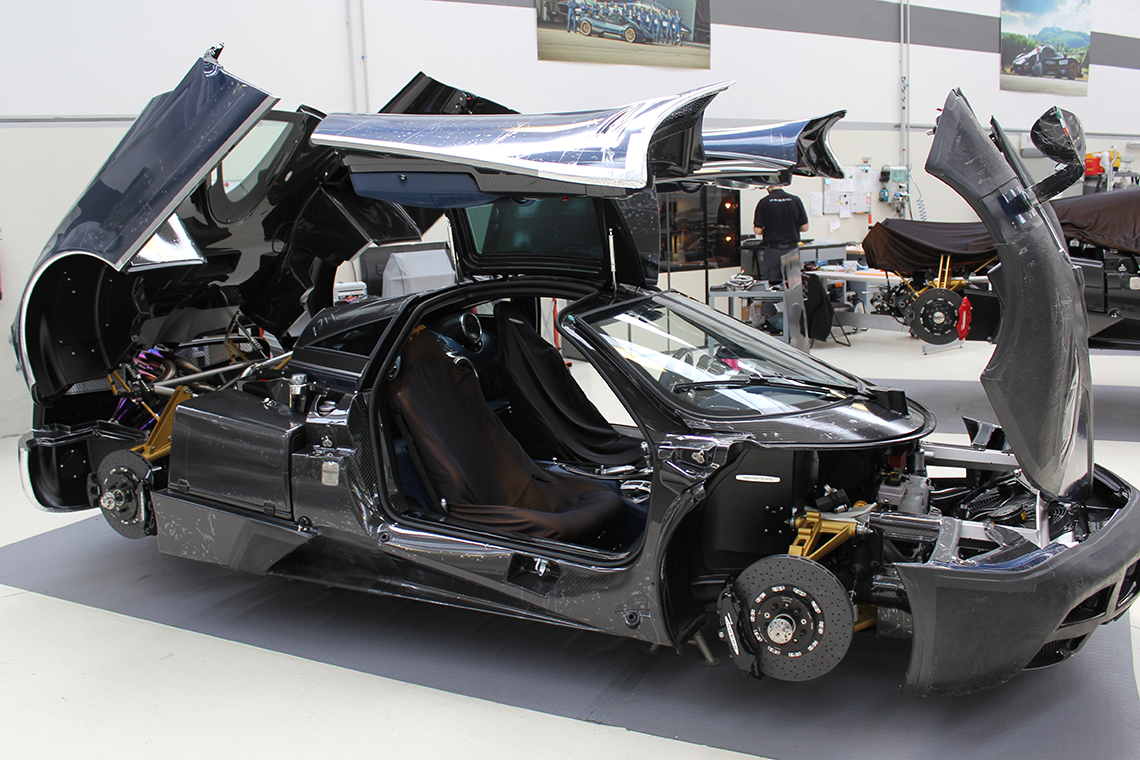 Pagani hypercar met deuren en motorkap open, toont interieur en motoronderdelen in een werkplaats.