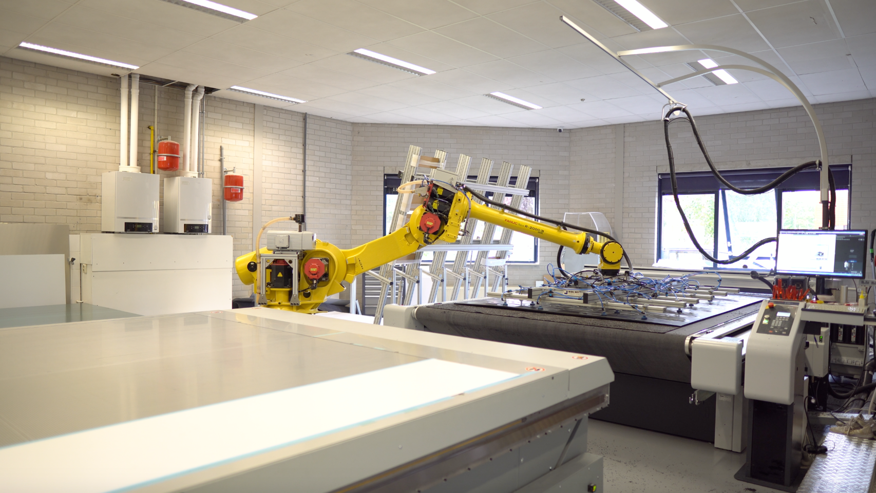 Gele robotarm van FANUC R-2000iB boven een snijtafel in een moderne werkplaats met witte bakstenen muren. Gele robotarm van FANUC R-2000iB boven een snijtafel in een moderne werkplaats met witte bakstenen muren.