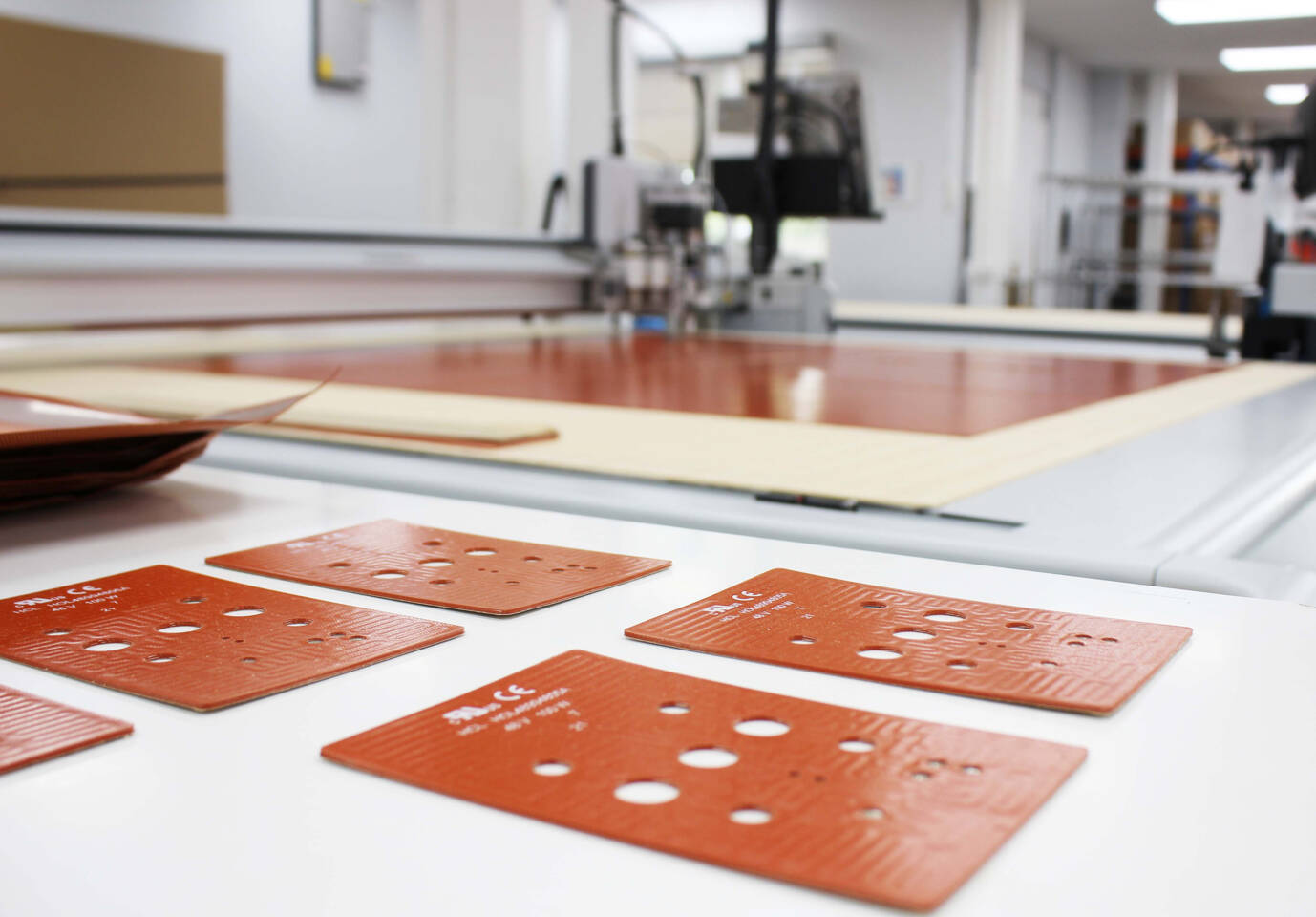 Several orange silicone heating elements with circular cutouts are laid out on a white surface, with a Z&uuml;nd cutting system in the background.