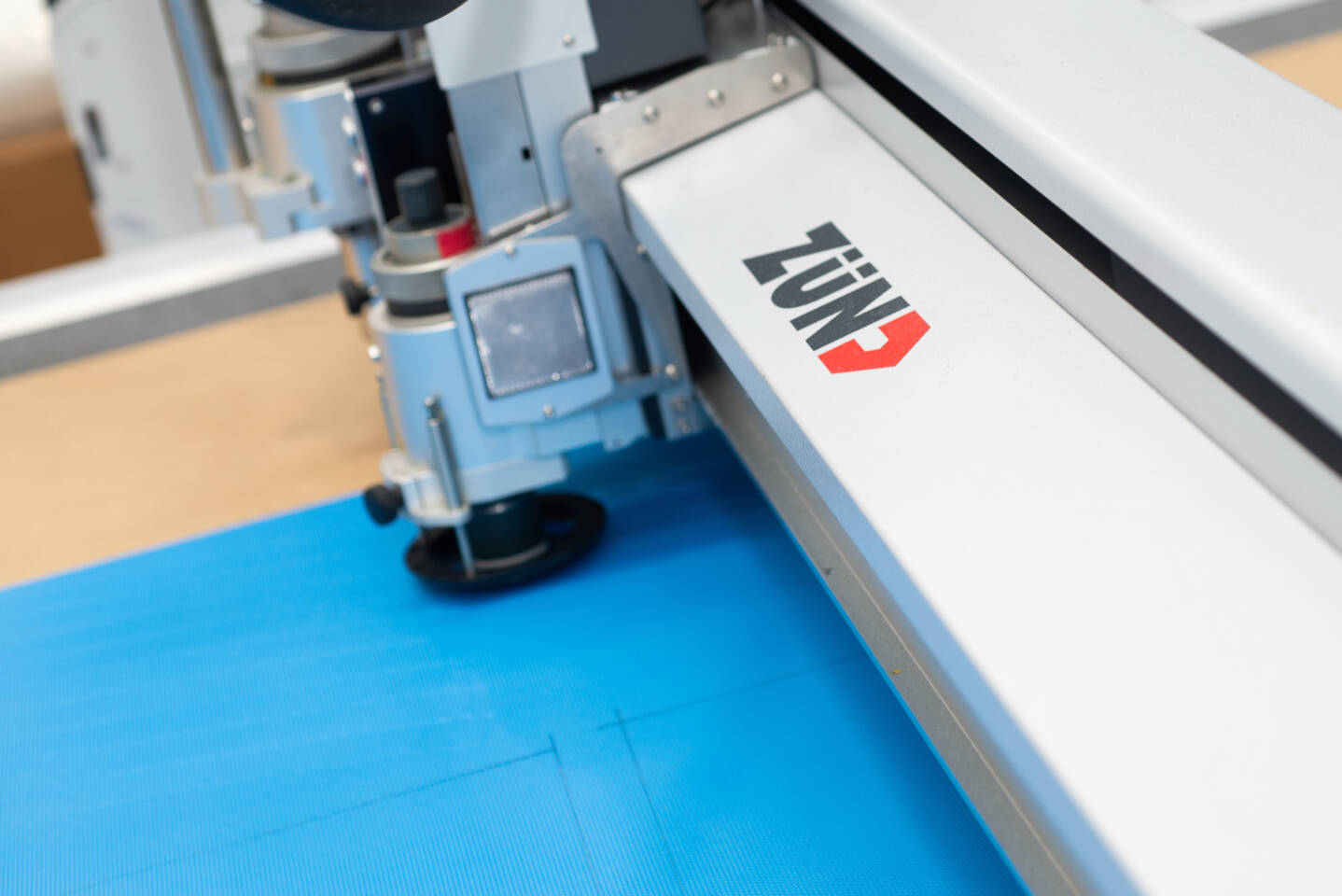 Close-up of a Z&uuml;nd cutting system with its logo, precisely cutting a blue material on a workbench.