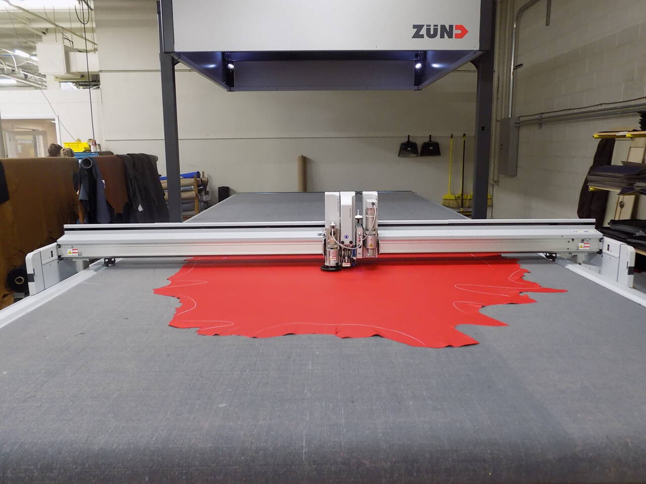 Z&uuml;nd Integra cutting system precisely cutting a red leather hide with white pattern outlines in a manufacturing facility.