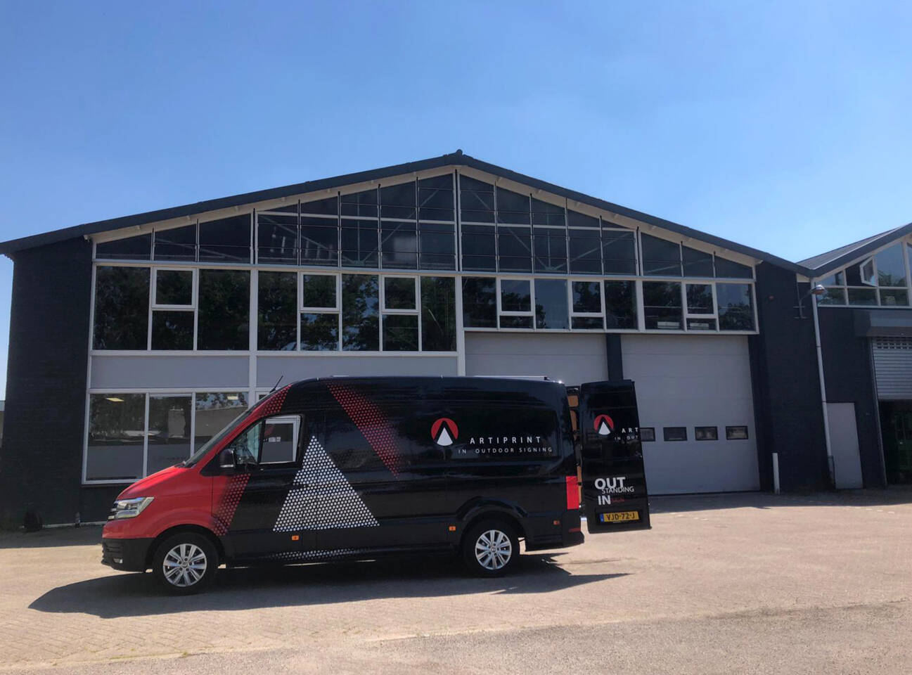 Bedrijfsbus van Artiprint voor buitensignalisatie geparkeerd voor een modern gebouw met grote ramen.