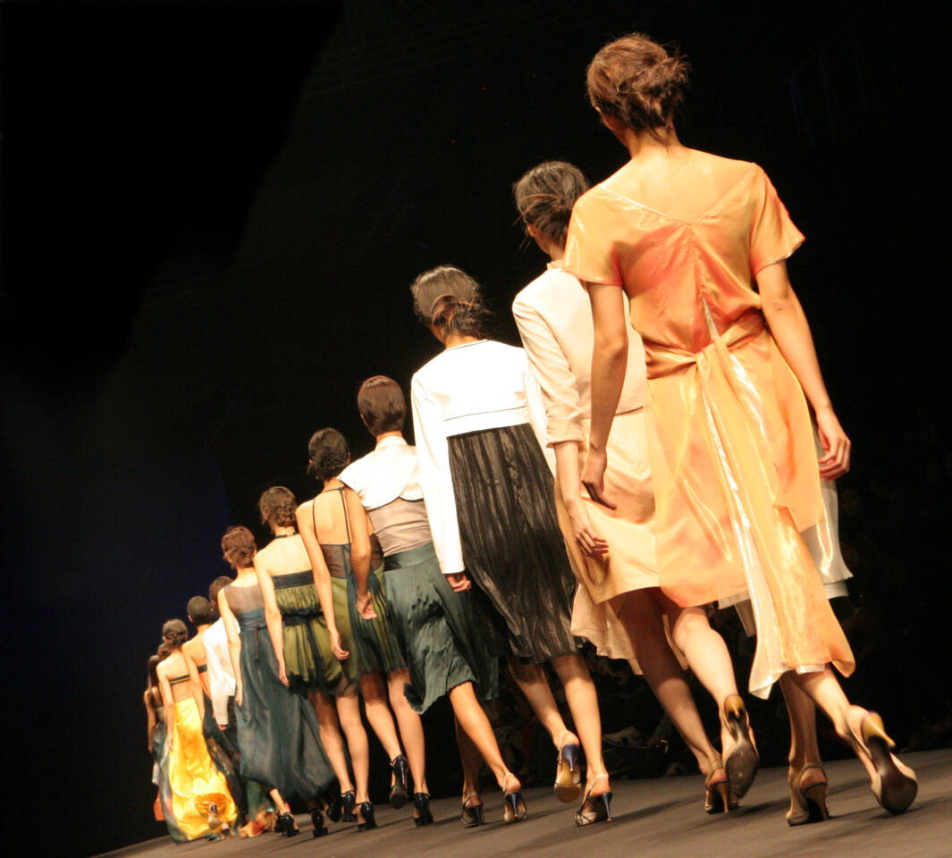 Modelle in abiti eleganti sfilano in passerella con abiti colorati su sfondo scuro, visti da dietro. Modelle in abiti eleganti sfilano in passerella con abiti colorati su sfondo scuro, visti da dietro.
