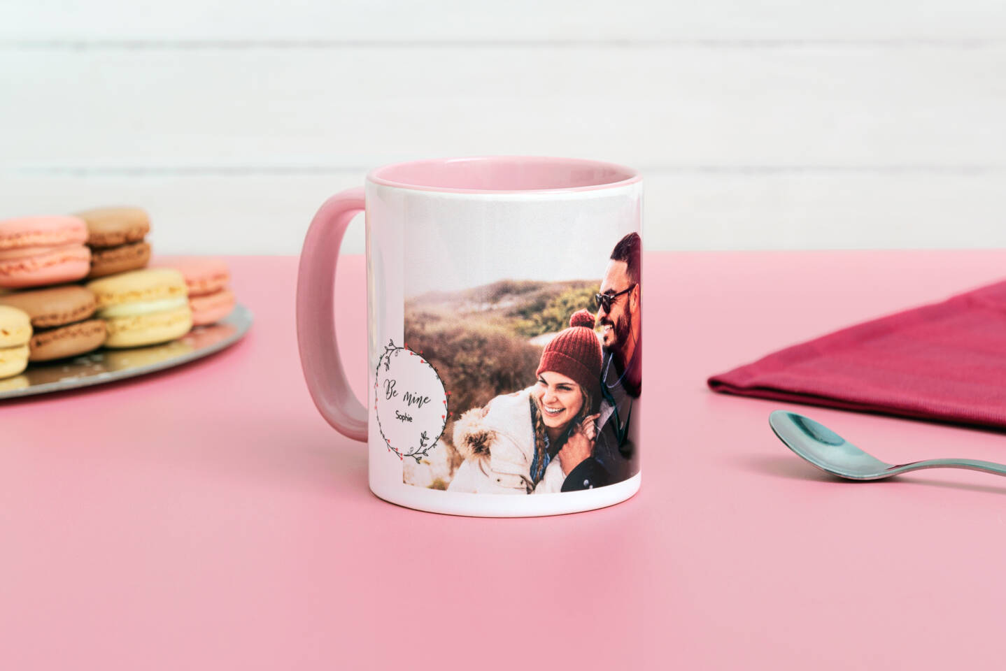 Roze mok met foto van een lachend stel, 'Be Mine Sophie' tekst en macarons op een roze tafel. Roze mok met foto van een lachend stel, 'Be Mine Sophie' tekst en macarons op een roze tafel.