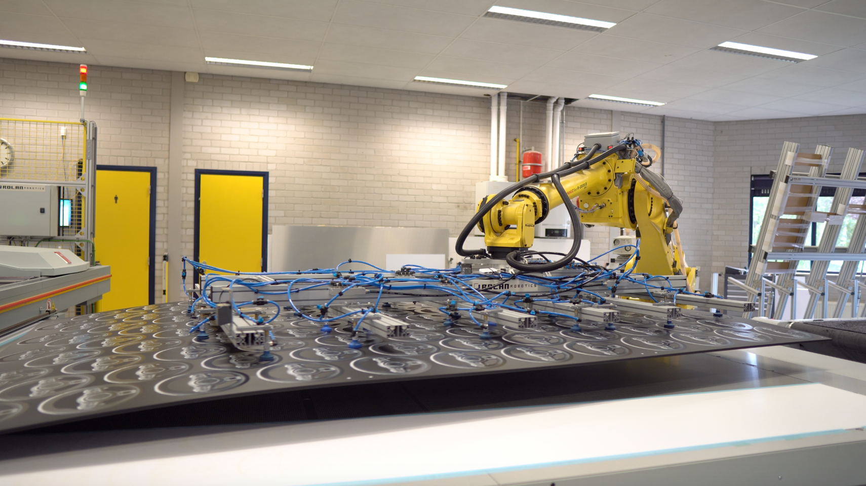 Gele robotarm met zuignappen op een zwart oppervlak met cirkels, verbonden met blauwe slangen in een fabriekshal. Gele robotarm met zuignappen op een zwart oppervlak met cirkels, verbonden met blauwe slangen in een fabriekshal.