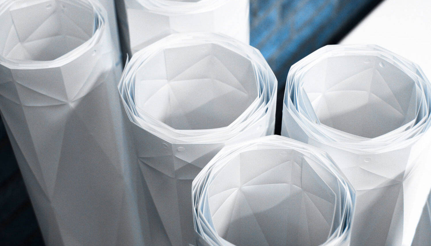Close-up of several rolled white paper sheets with faceted geometric patterns, standing upright. Close-up of several rolled white paper sheets with faceted geometric patterns, standing upright.