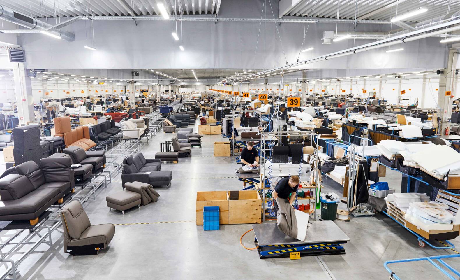Große Fabrikhalle mit vielen Sofas und Möbelteilen in der Produktion, Arbeiter sind beschäftigt. Große Fabrikhalle mit vielen Sofas und Möbelteilen in der Produktion, Arbeiter sind beschäftigt.