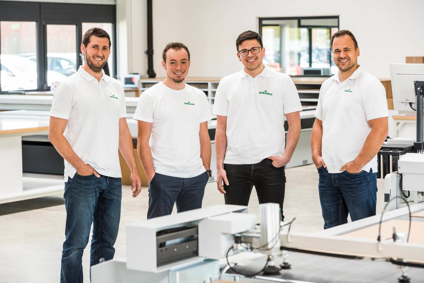 Vier l&auml;chelnde M&auml;nner in wei&szlig;en Poloshirts mit dem Zerhusen-Logo stehen in einem hellen B&uuml;roumfeld.
