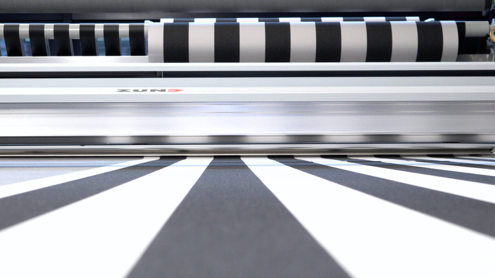 Zünd Systemtechnik cutter processing striped material, showing the precision cutting head and the striped fabric being fed through. Zünd Systemtechnik cutter processing striped material, showing the precision cutting head and the striped fabric being fed through.