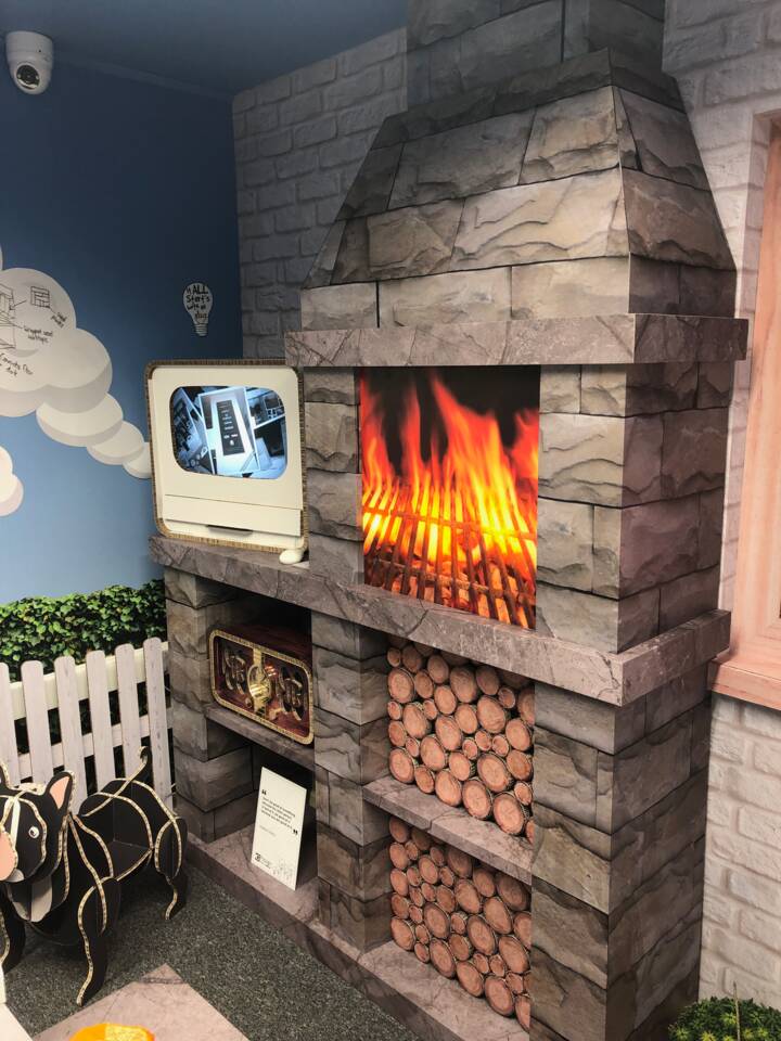 A decorative fireplace with a digital screen showing a product display, next to a vibrant flame graphic and stacked logs.