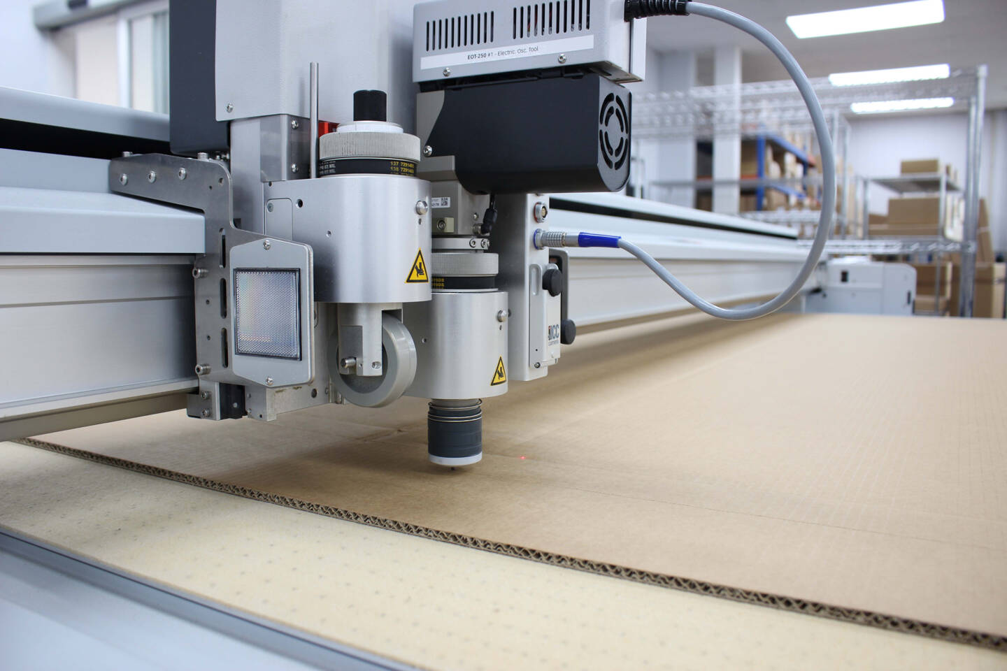 Z&uuml;nd cutting system with a laser projection system precisely cutting corrugated cardboard in a warehouse environment.