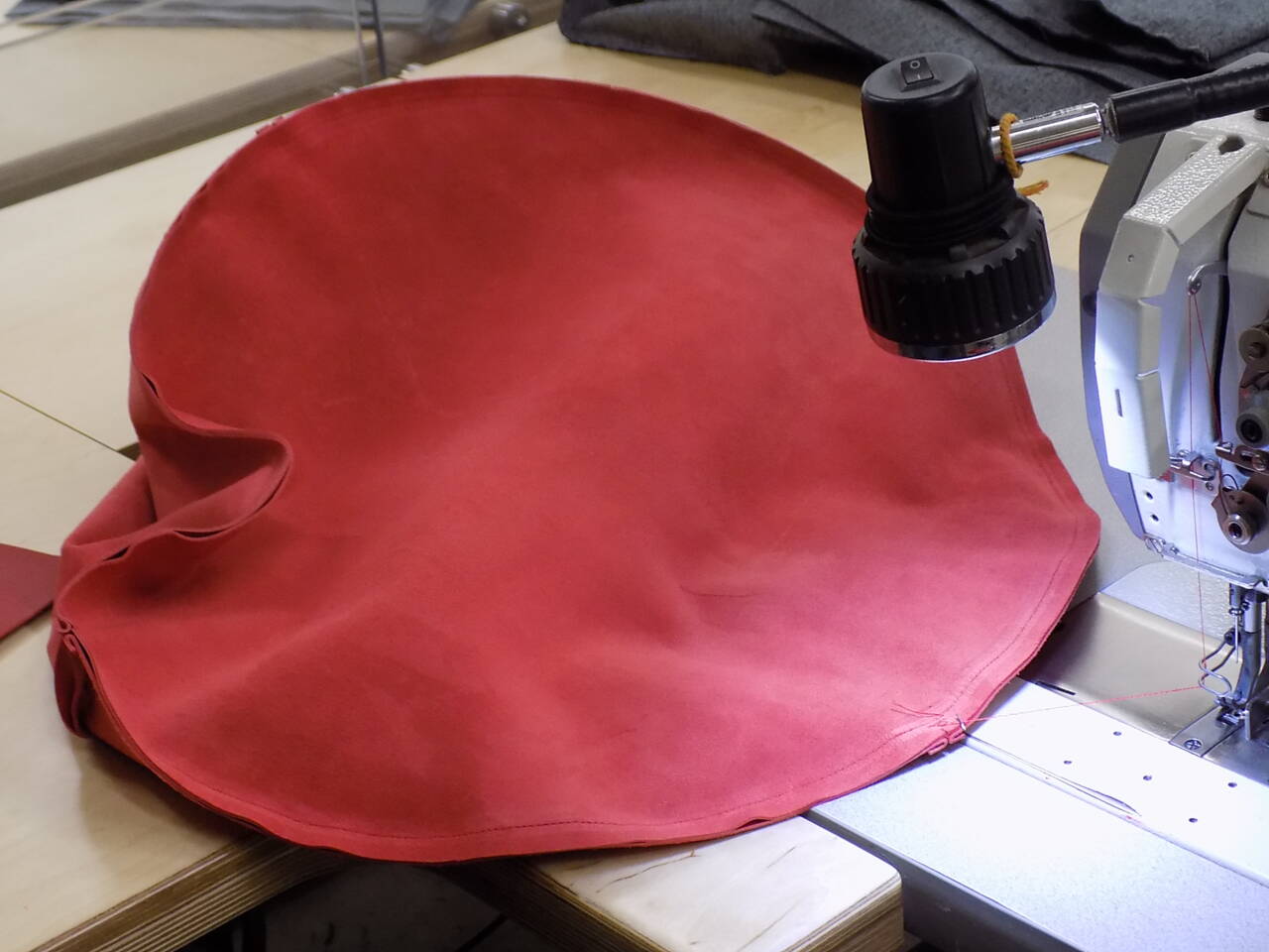 A red piece of leather is being sewn on a Z&uuml;nd system with an overhead light and sewing machine details visible.